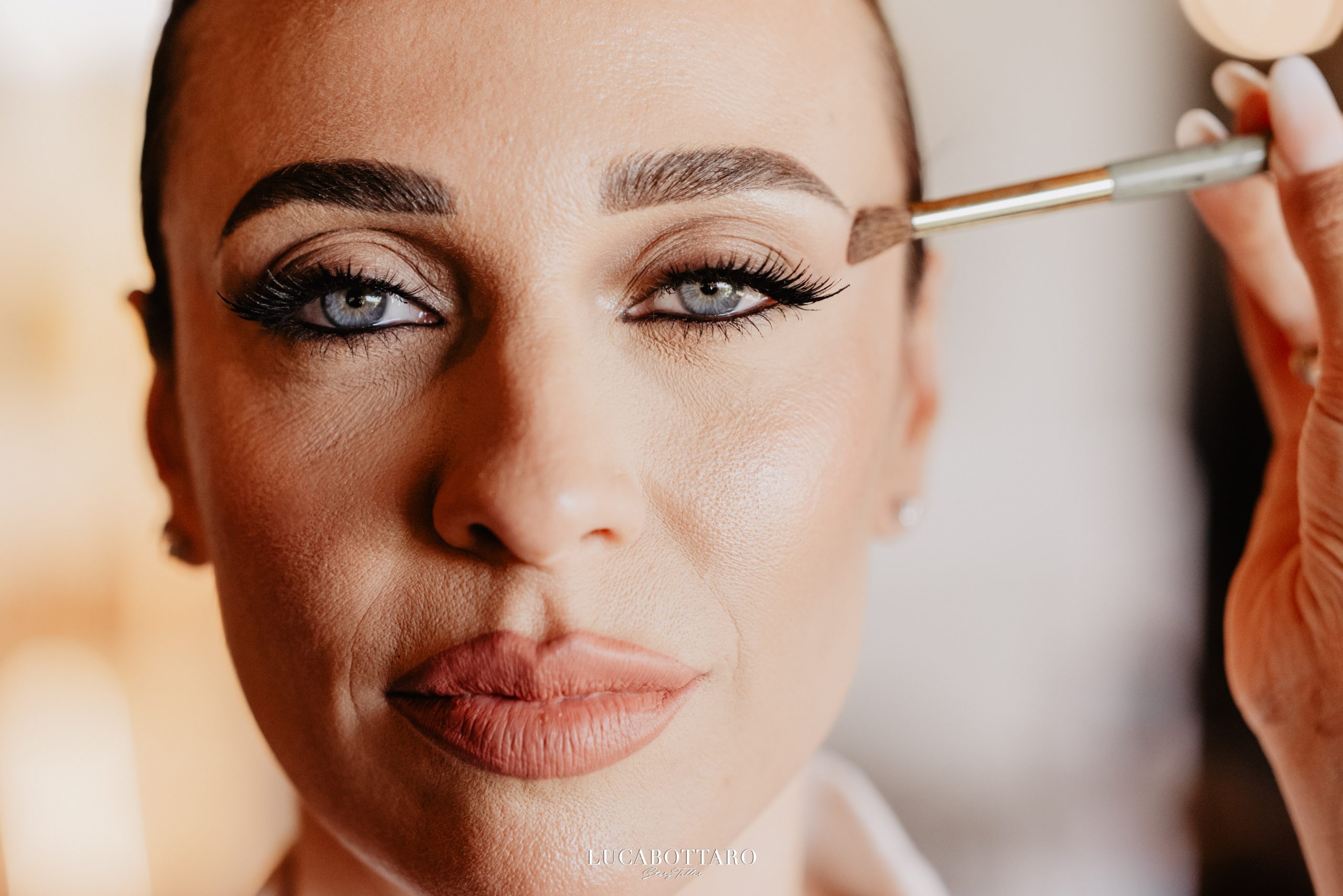 Primo piano di trucco sposa in preparazione, make-up artist applica ombretto con pennello sull'occhio