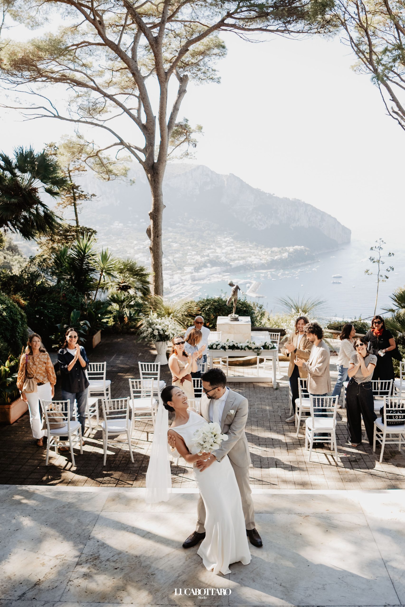 Bride and groom dancing on a terrace in Capri as guests applaud, with the sea and cliffs behind them