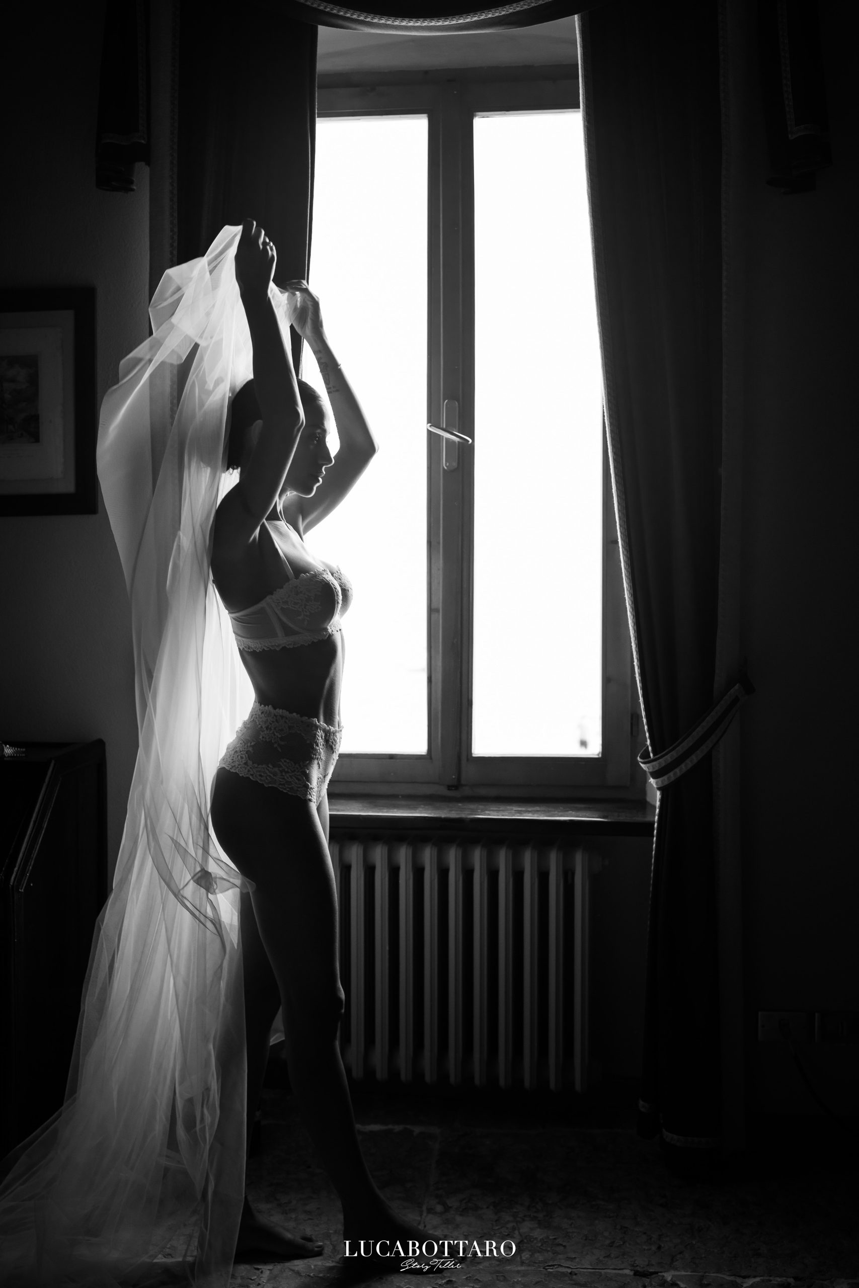 Sposa in camicia bianca seduta su una poltrona, che sorride mentre si sistema il sandalo, nella camera storica